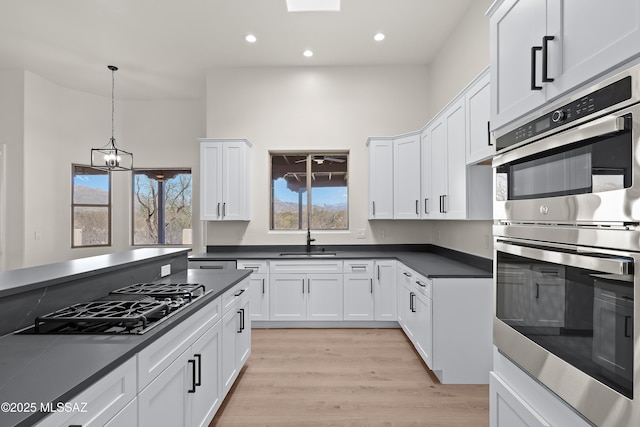 kitchen with dark countertops, black gas stovetop, stainless steel double oven, white cabinets, and a sink