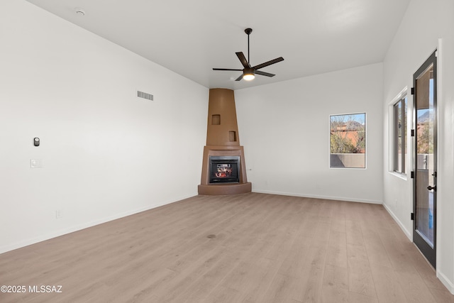 unfurnished living room featuring visible vents, a large fireplace, baseboards, ceiling fan, and light wood-style flooring