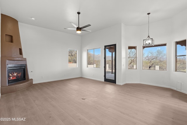 unfurnished living room with light wood finished floors, a ceiling fan, a large fireplace, and baseboards