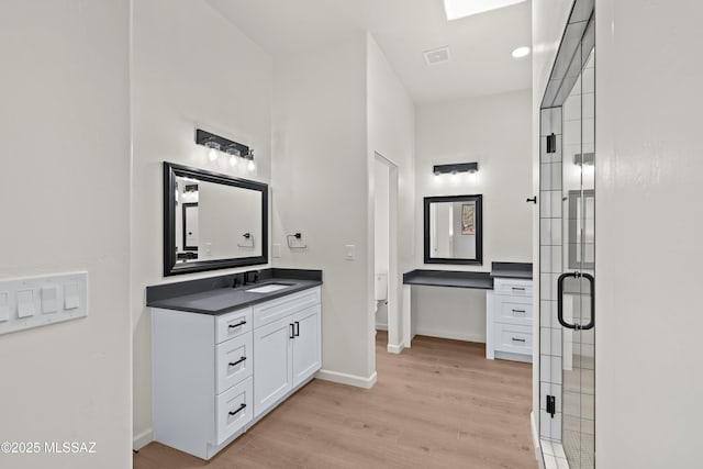 full bath featuring visible vents, a stall shower, wood finished floors, baseboards, and vanity