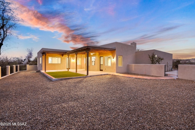 rear view of property featuring stucco siding, fence private yard, a patio, and a gate