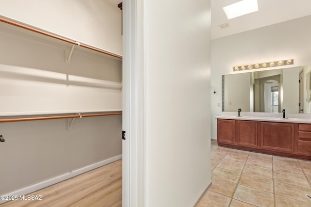 full bathroom with baseboards, double vanity, a skylight, a sink, and a walk in closet