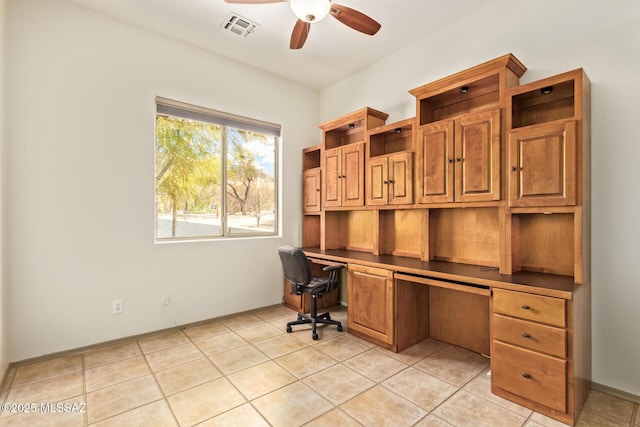 unfurnished office with visible vents, built in desk, light tile patterned floors, baseboards, and ceiling fan