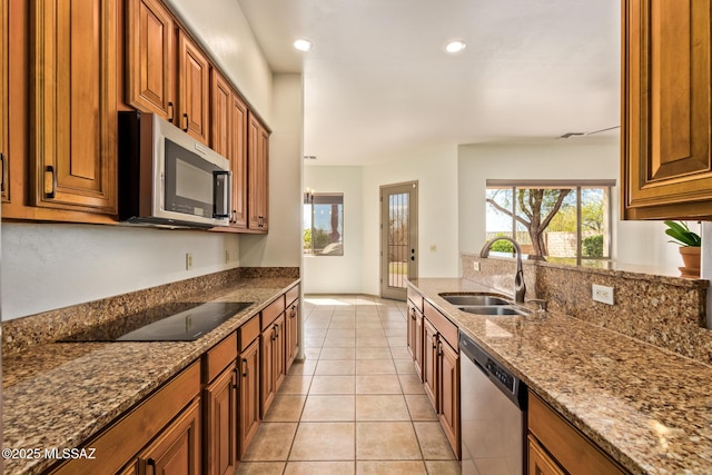 kitchen with dark stone countertops, brown cabinets, appliances with stainless steel finishes, light tile patterned flooring, and a sink