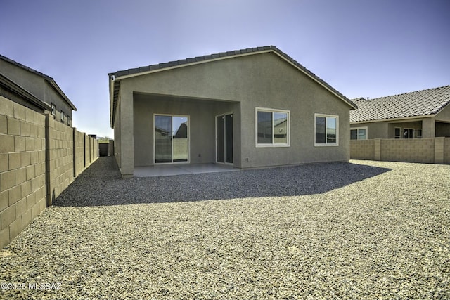 rear view of house featuring stucco siding, a patio, a tile roof, and a fenced backyard