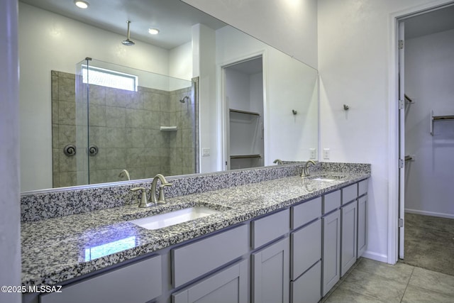 full bath with double vanity, a spacious closet, a tile shower, and a sink