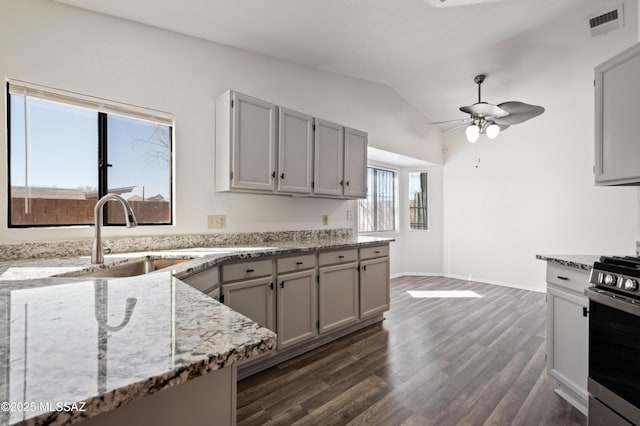 kitchen with light stone countertops, stainless steel gas range, dark wood finished floors, lofted ceiling, and a sink