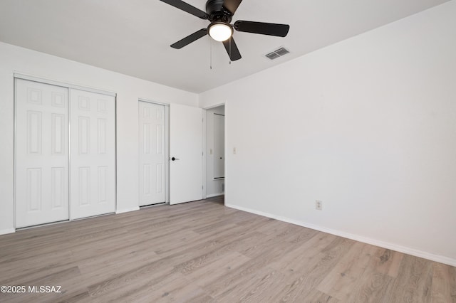 unfurnished bedroom featuring visible vents, baseboards, multiple closets, and wood finished floors