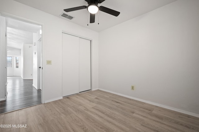 unfurnished bedroom with a closet, visible vents, baseboards, and wood finished floors