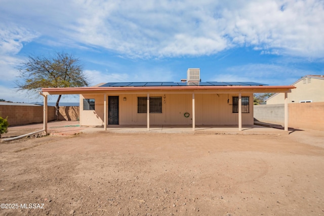 rear view of house featuring roof mounted solar panels, a fenced backyard, and a patio area