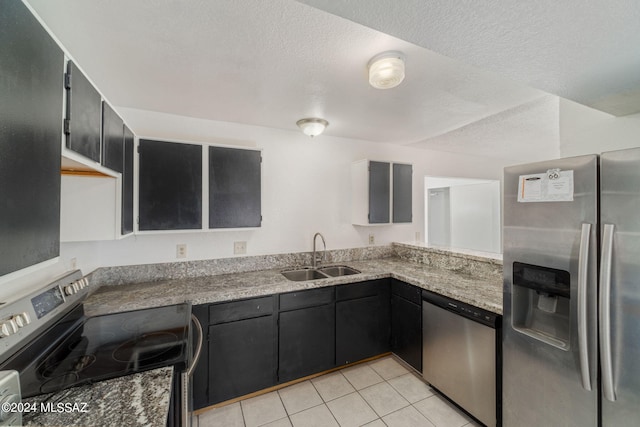 kitchen featuring light tile patterned floors, stainless steel appliances, dark cabinetry, a textured ceiling, and a sink