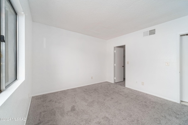 spare room with visible vents, carpet floors, a textured ceiling, and baseboards