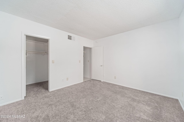 unfurnished bedroom featuring visible vents, carpet, a walk in closet, and a textured ceiling