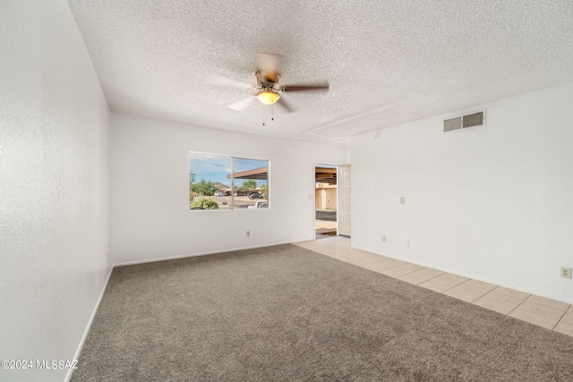 spare room featuring a ceiling fan, visible vents, light tile patterned flooring, a textured ceiling, and light carpet