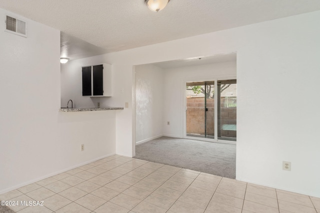 carpeted empty room with tile patterned floors, baseboards, visible vents, and a textured ceiling