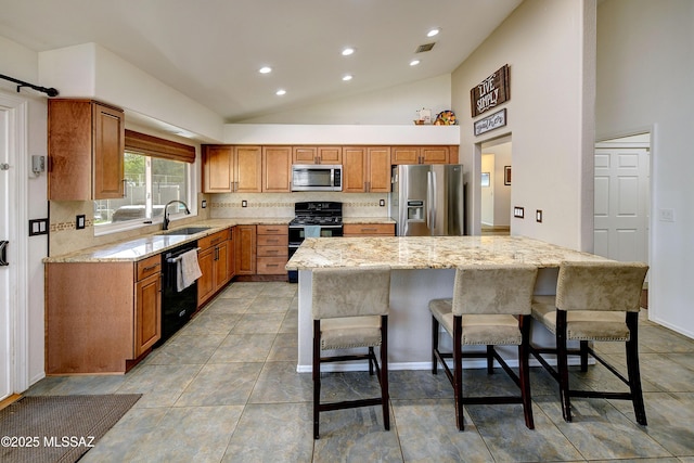 kitchen featuring tasteful backsplash, light stone counters, a kitchen breakfast bar, black appliances, and a sink