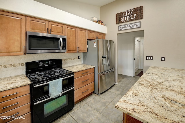 kitchen with light tile patterned floors, light stone countertops, tasteful backsplash, and appliances with stainless steel finishes