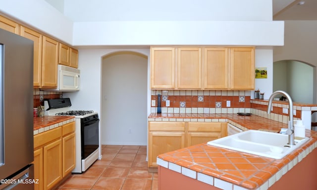 kitchen with white appliances, light brown cabinets, arched walkways, and a sink