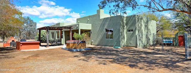 rear view of house with stucco siding, a pergola, and fence