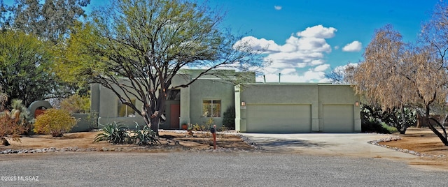 adobe home featuring a garage, concrete driveway, and stucco siding