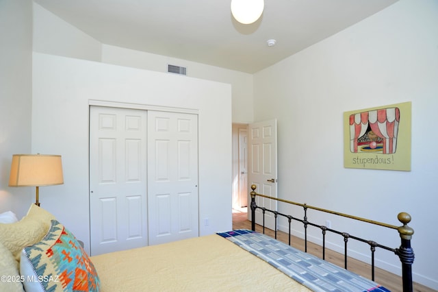 bedroom with wood finished floors, visible vents, a closet, and baseboards