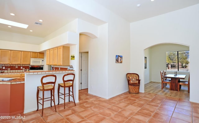 kitchen with visible vents, tasteful backsplash, tile countertops, white microwave, and a towering ceiling