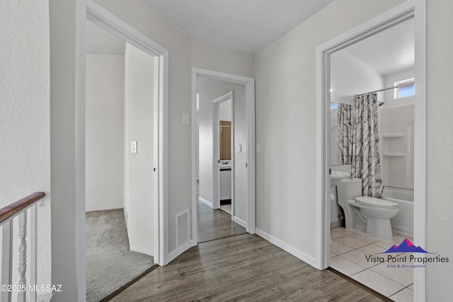 hallway with visible vents, baseboards, and wood finished floors