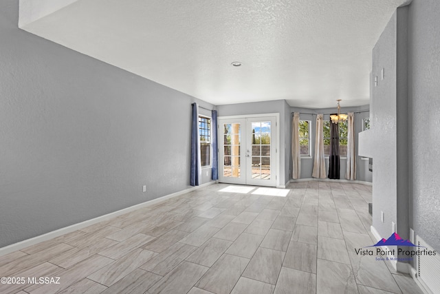 unfurnished room with a notable chandelier, a textured ceiling, french doors, baseboards, and a textured wall