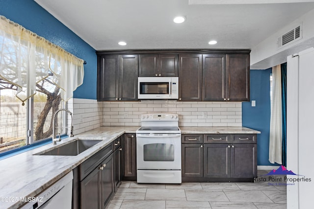 kitchen with visible vents, backsplash, dark brown cabinetry, white appliances, and a sink