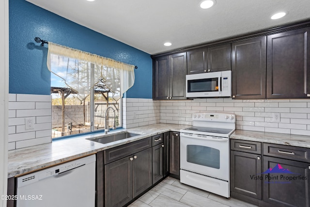 kitchen featuring a sink, white appliances, light stone counters, and a textured wall