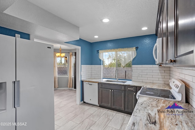 kitchen with a sink, white appliances, plenty of natural light, and a chandelier