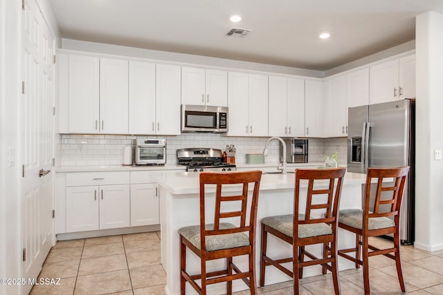 kitchen featuring stainless steel appliances, visible vents, decorative backsplash, and light countertops