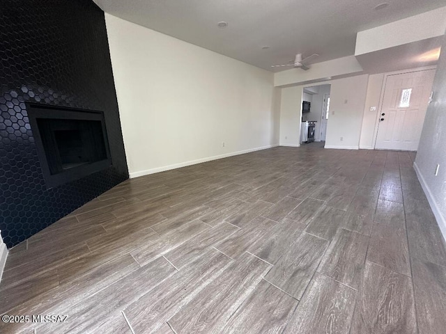 unfurnished living room featuring baseboards, a ceiling fan, wood finished floors, and a fireplace