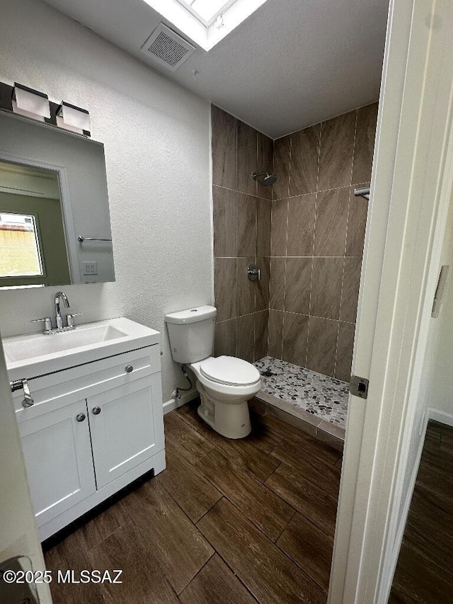 full bath featuring vanity, wood finished floors, visible vents, a tile shower, and toilet