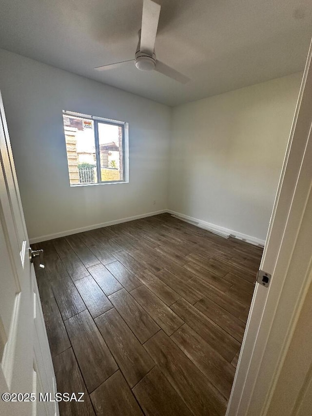 spare room featuring baseboards, dark wood-type flooring, and a ceiling fan