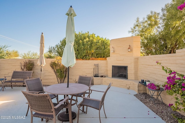 view of patio / terrace featuring exterior fireplace, outdoor dining area, and a fenced backyard