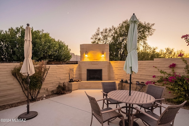 patio terrace at dusk featuring outdoor dining space, fence, and an outdoor fireplace