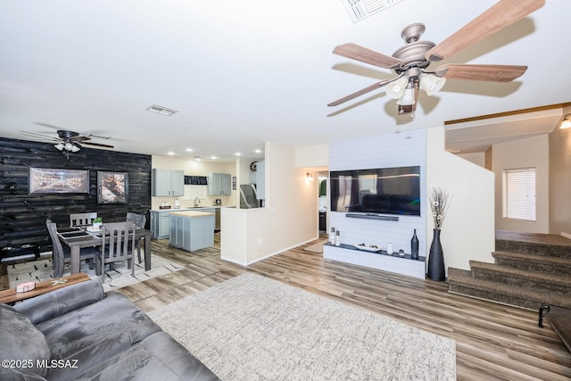 living area with stairway, a ceiling fan, visible vents, and light wood finished floors