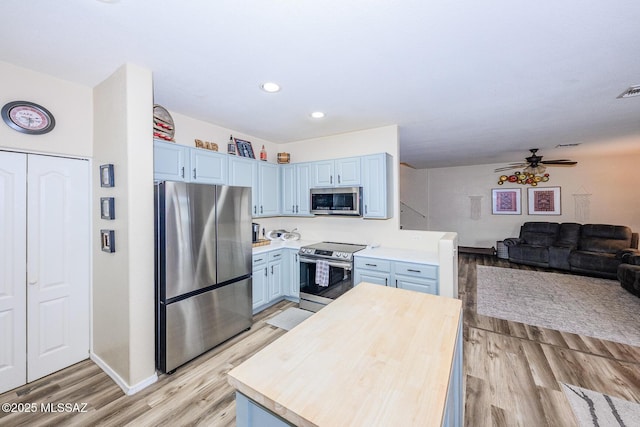 kitchen featuring a ceiling fan, open floor plan, stainless steel appliances, light wood finished floors, and wooden counters