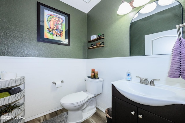 half bath with vanity, toilet, wood finished floors, and a wainscoted wall