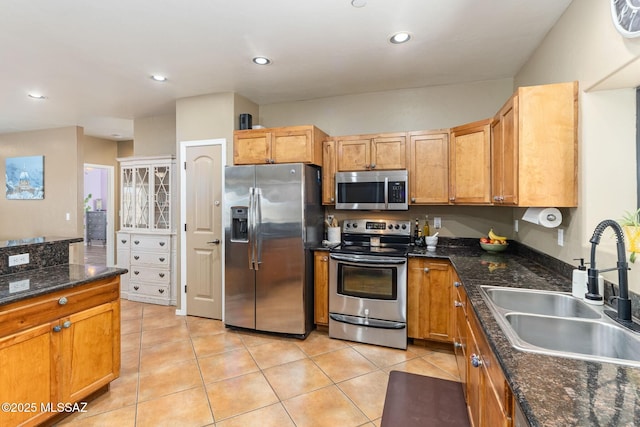 kitchen featuring a sink, recessed lighting, dark stone counters, appliances with stainless steel finishes, and light tile patterned flooring