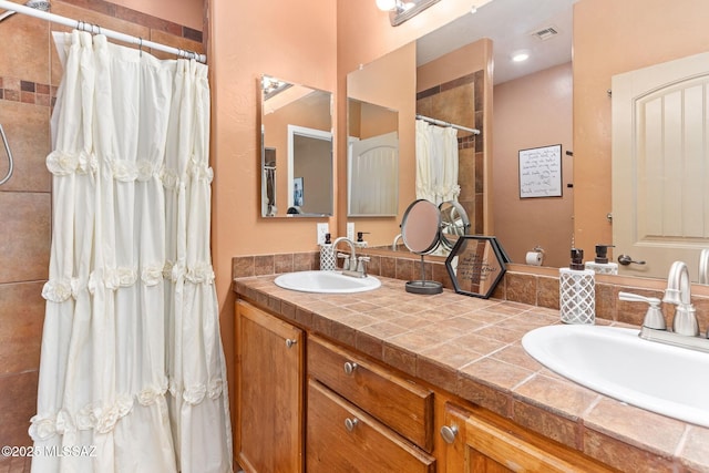 bathroom featuring double vanity, tiled shower, visible vents, and a sink