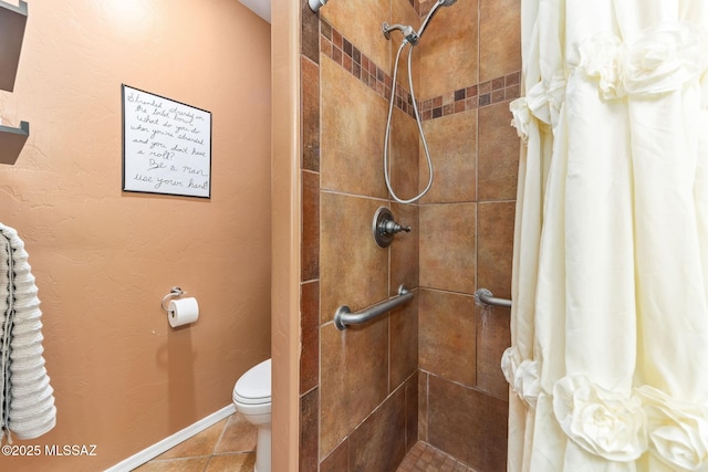 bathroom with tile patterned floors, toilet, baseboards, and a tile shower