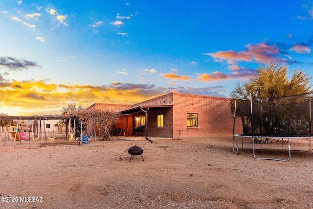 back of property at dusk with brick siding, a fire pit, playground community, and a trampoline