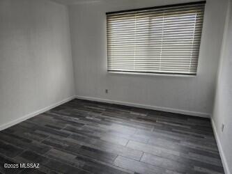 spare room featuring baseboards and dark wood-style flooring