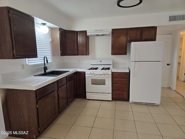 kitchen with under cabinet range hood, dark brown cabinetry, light tile patterned flooring, white appliances, and a sink