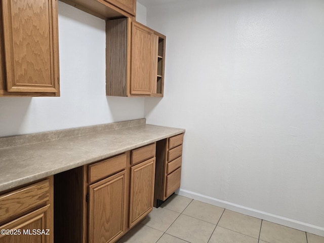 kitchen with light countertops, light tile patterned flooring, brown cabinetry, and baseboards