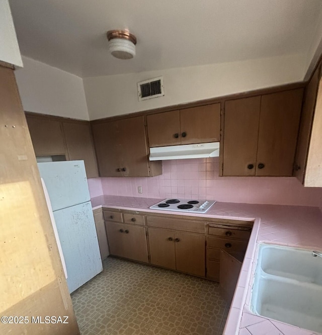 kitchen with visible vents, under cabinet range hood, tile countertops, white appliances, and a sink