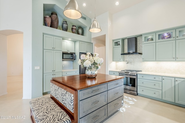 kitchen featuring wall chimney range hood, butcher block countertops, a high ceiling, arched walkways, and stainless steel appliances