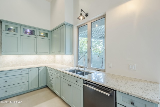 kitchen with a sink, glass insert cabinets, decorative backsplash, light stone countertops, and dishwasher